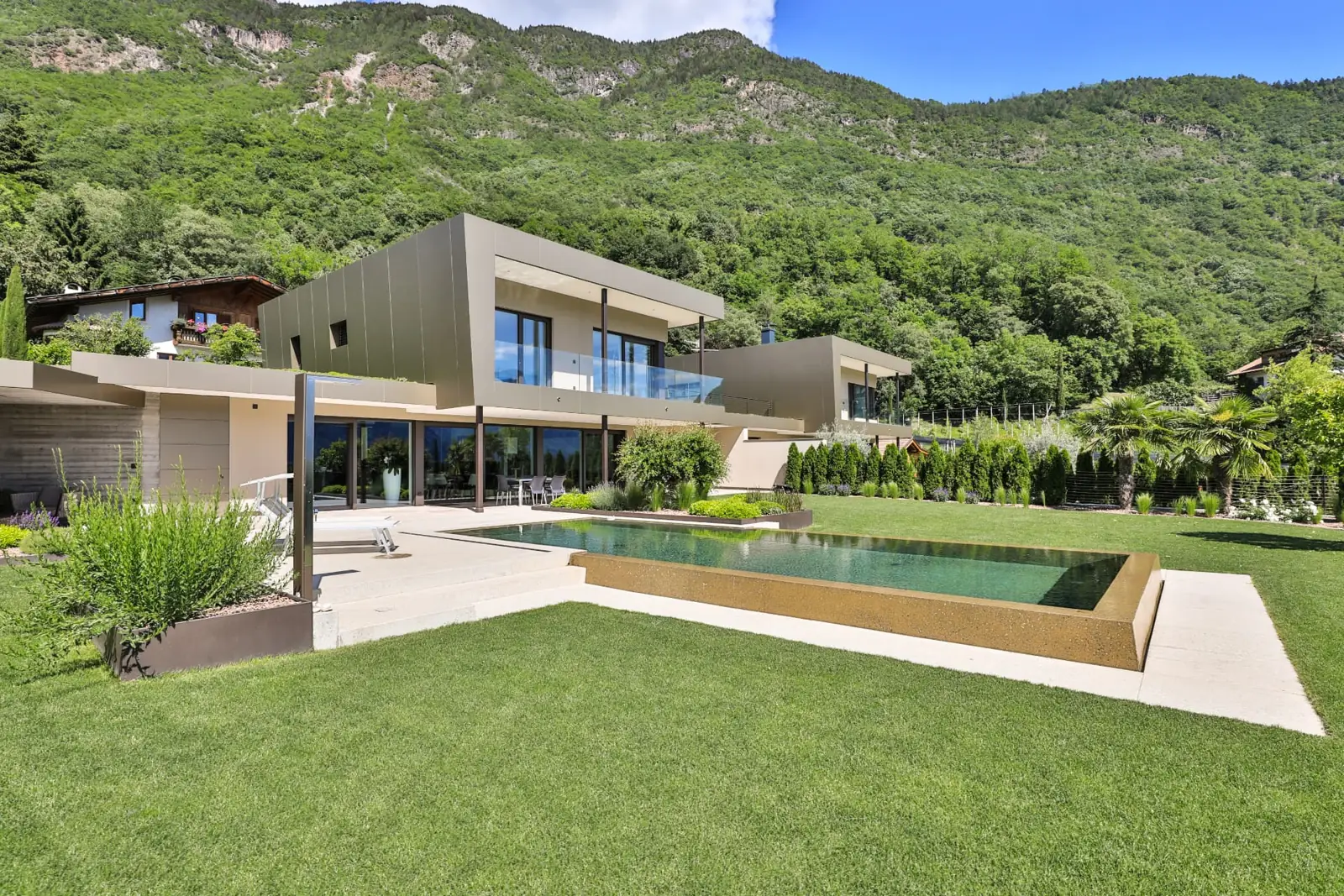 Villa R Burgstall — Gartenansicht der Villa mit Infinity-Pool vor bewaldetem Hang
