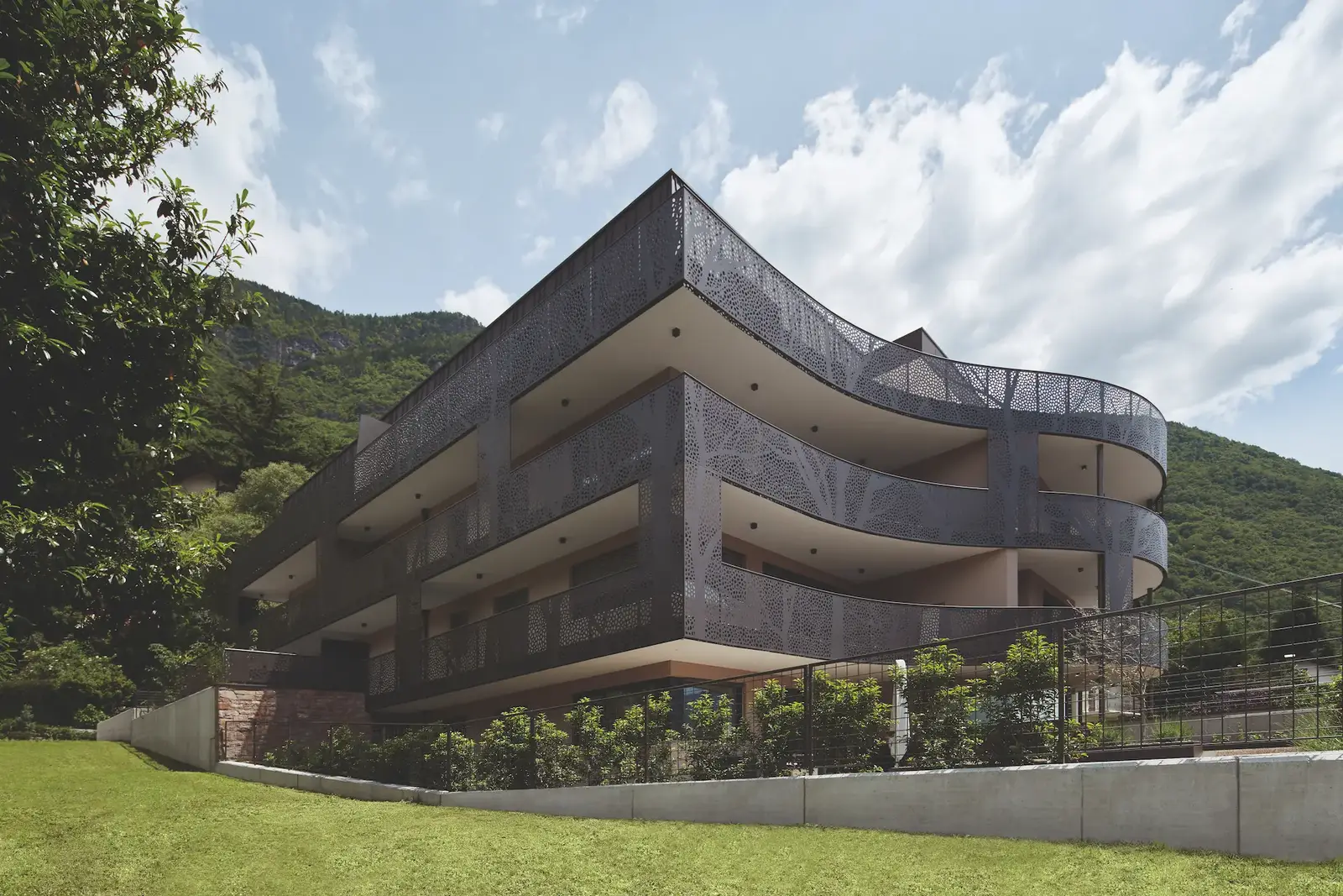Residence Waldele Burgstall — Außenansicht mit geschwungener, ornamental perforierter Balkonverkleidung und Bergkulisse