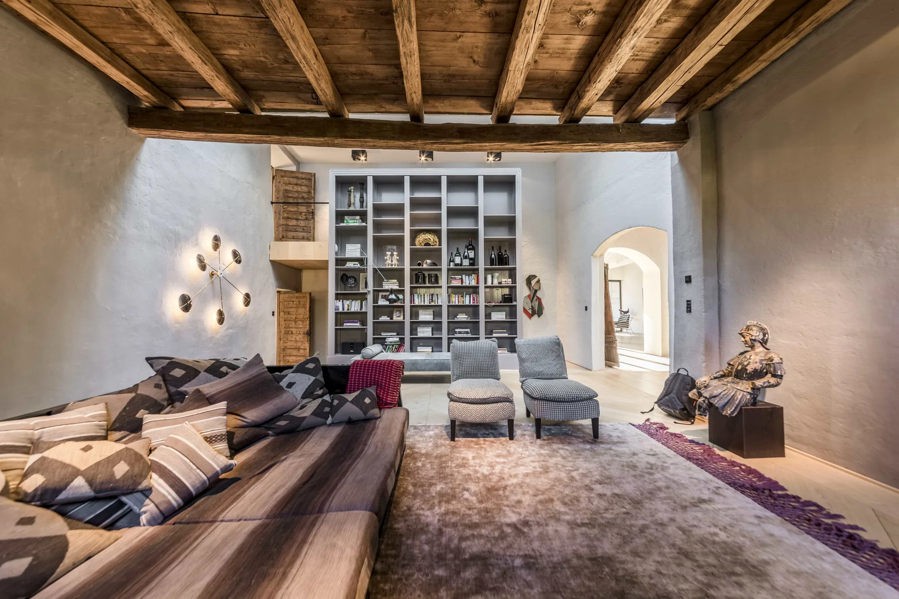 Historischer Wohnraum mit alter Holzbalkendecke, weißem Einbauregal und großem Sofa mit gemusterten Kissen